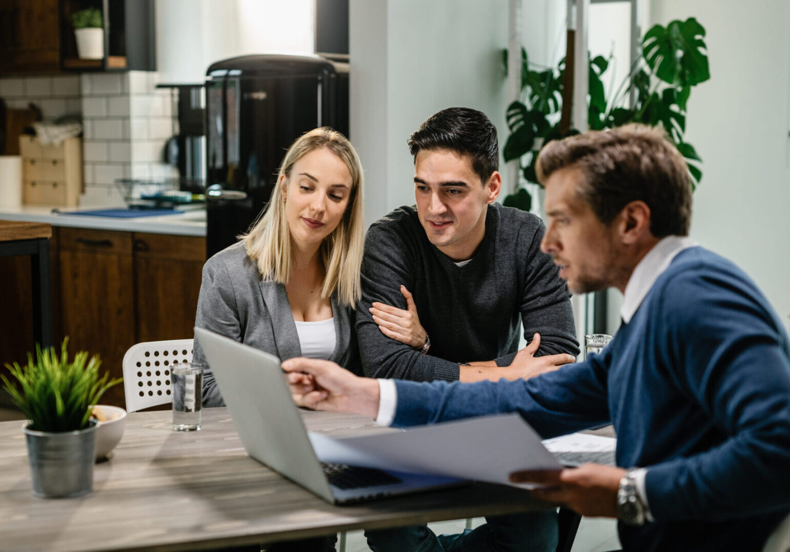 Young couple and real estate agent using laptop while going through housing plan on a meeting.